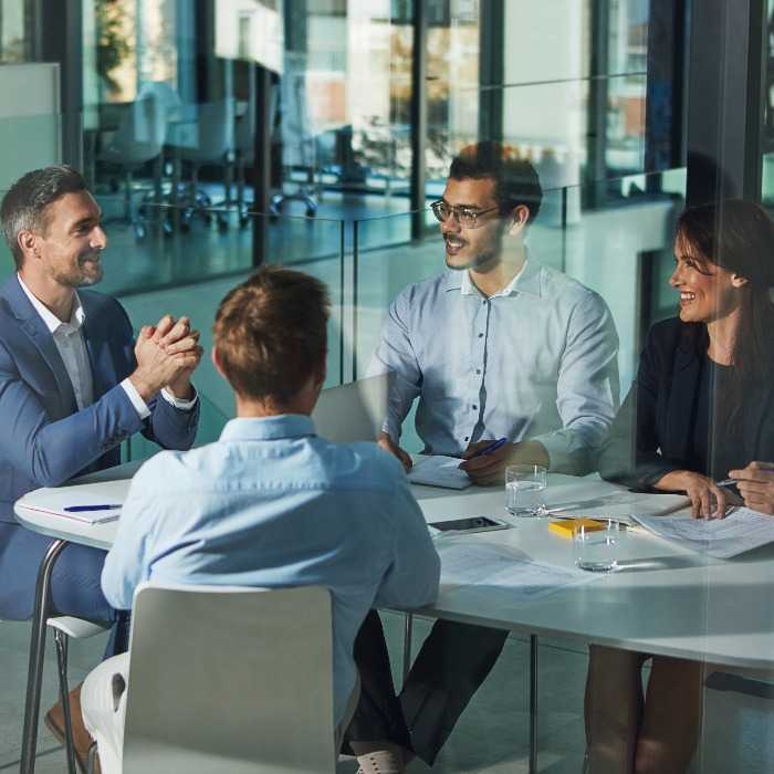 Group of four people discussing and smiling at a conference table full of papers