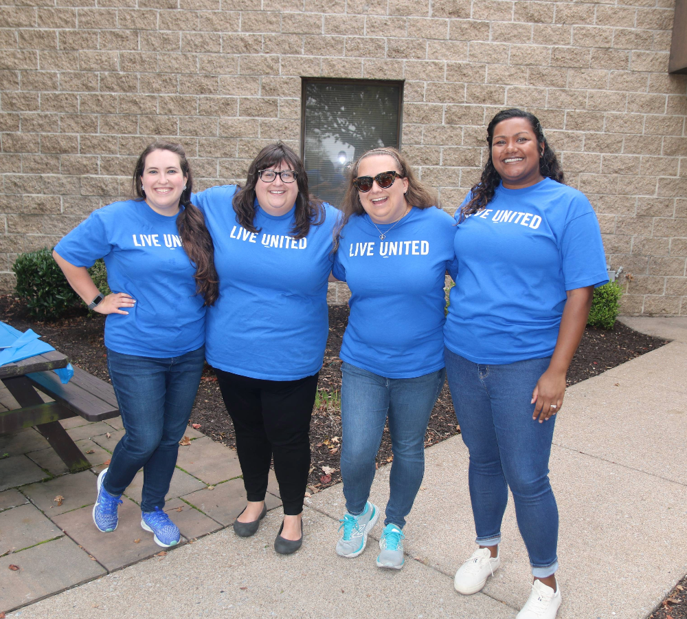 Four Brown Plus team members smiling with arms around each other in matching blue t-shirts