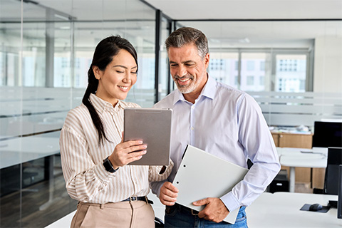 A man and woman standing next to each other looking over something on a tablet