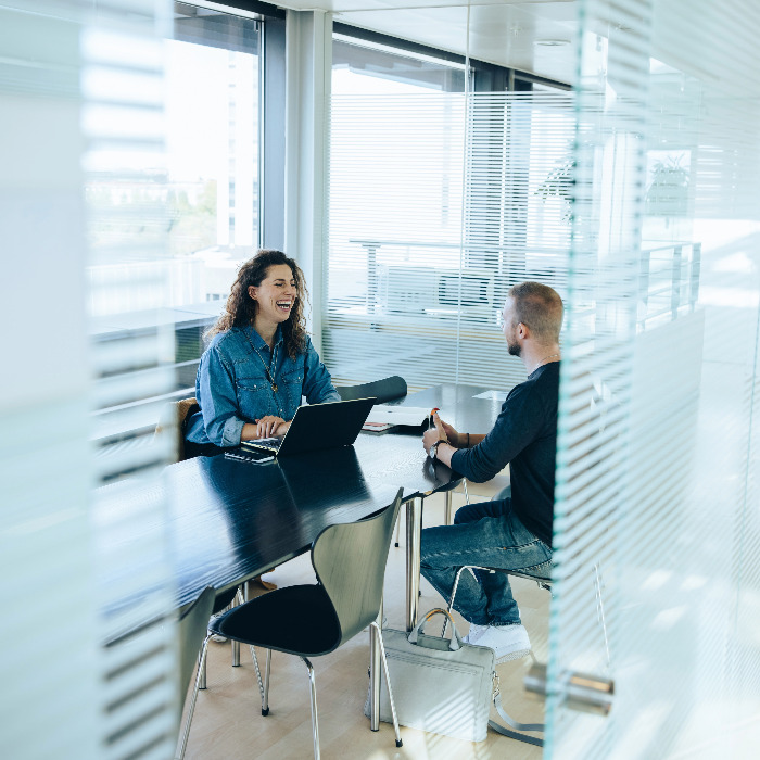 A woman in a blue shirt across the table from a man in a room with glass walls