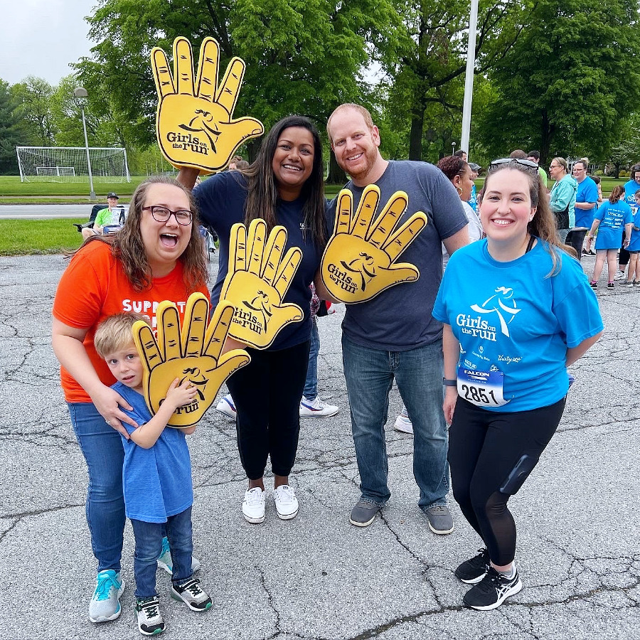 Four Brown Plus team members smiling and holding large yellow form hands