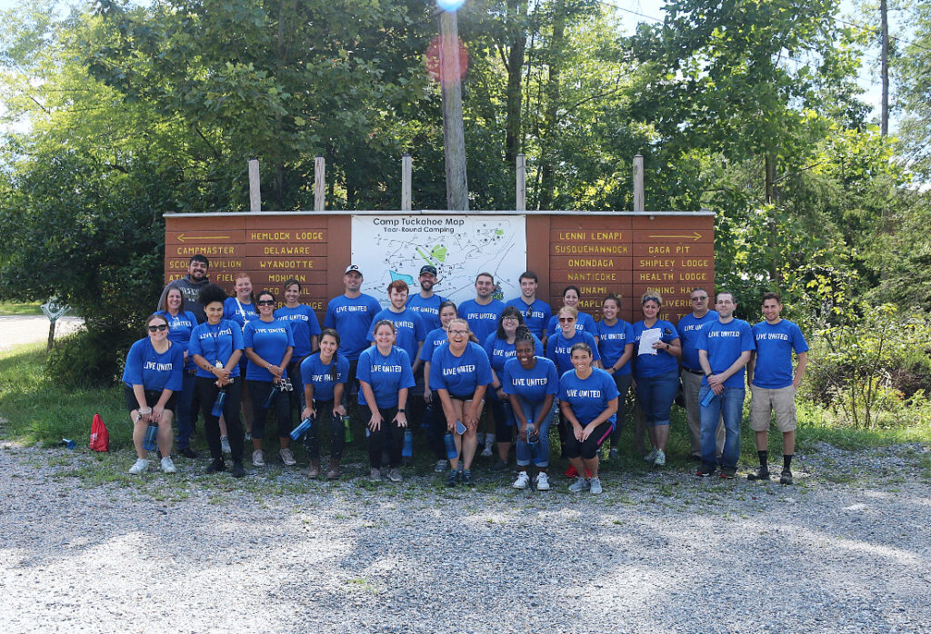 Group of Brown Plus team members in matching blue shirts posing in front of a trail map