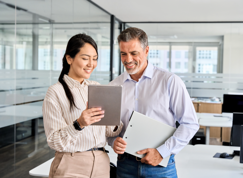 A man and woman standing next to each other looking over something on a tablet