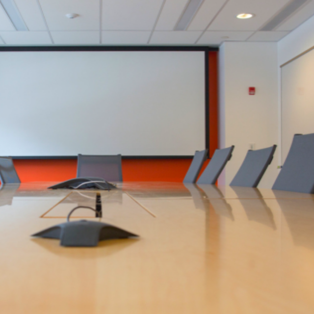 A conference room table with chairs around it and a projector screen on a wall