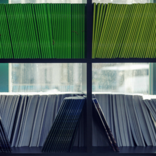 Shelves full of thin books with spines of blue, green, and yellow colors, grouped together