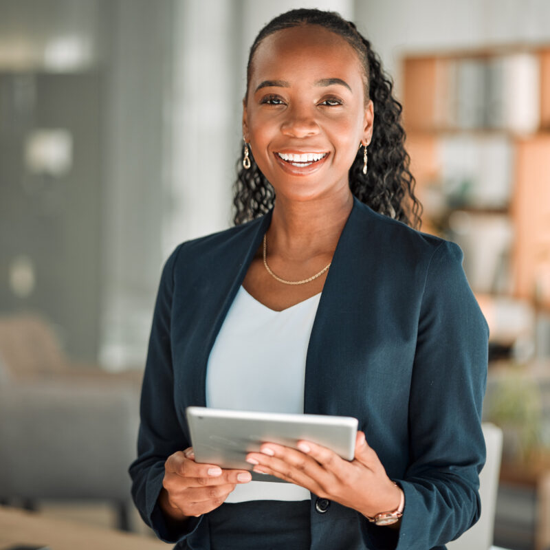 A woman smiling and standing holding a tablet wearing a dark blue blazer